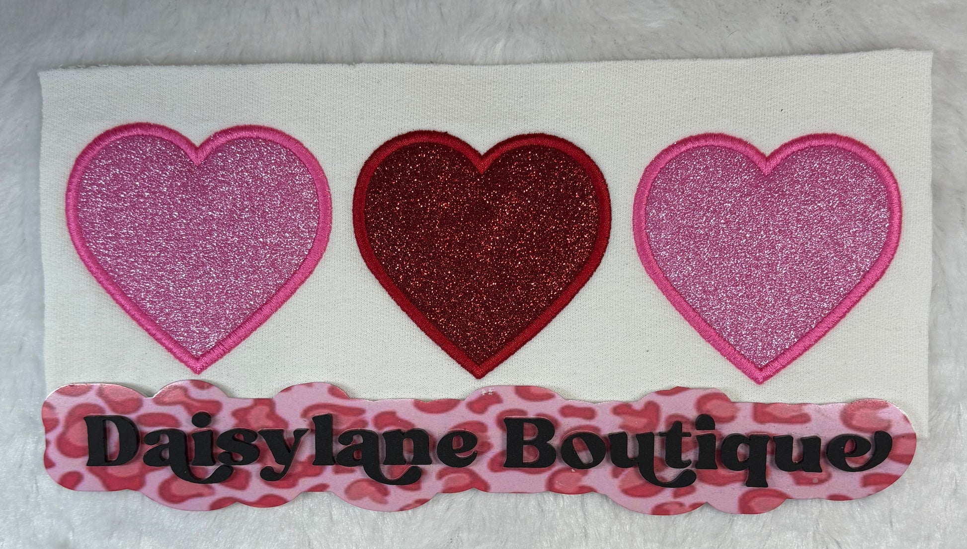 Three heart-shaped patches with glittery finish on a white background, featuring 'Daisy Lane Boutique' branding.