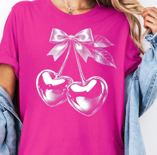 Pink t-shirt with white cherry design and bow on a person wearing denim jacket.
