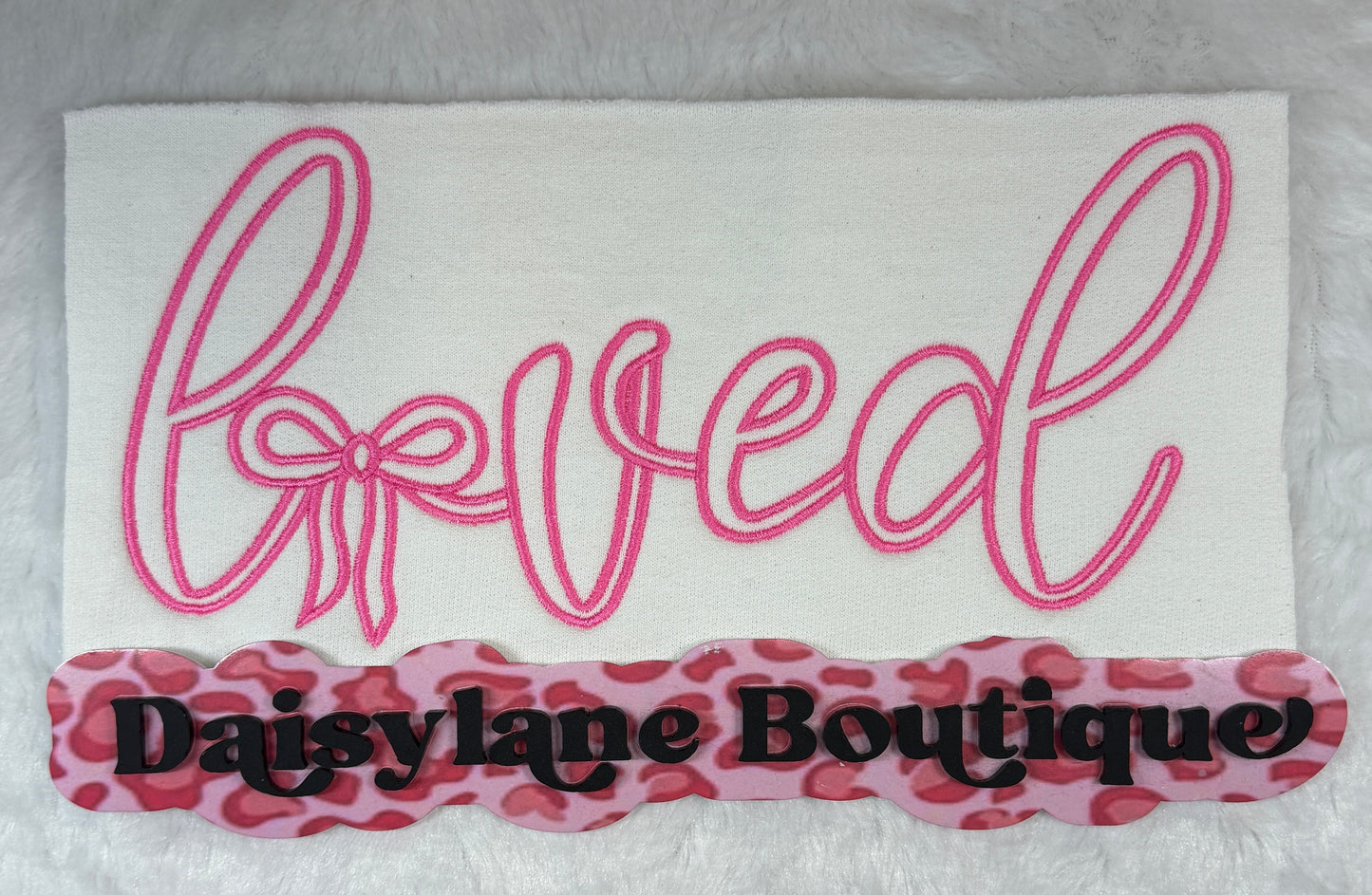 Fabric with 'loved' in pink cursive text and 'Daisylane Boutique' in black on a white background